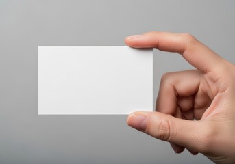 Fototapeta premium A close up view of a person holding a blank white business card against a neutral grey background