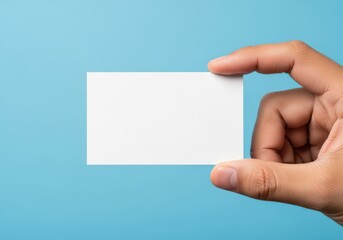 Obraz premium A hand holding a blank white business card against a plain light blue background for branding