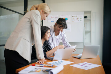 Fototapeta premium Three women collaborating on a business project, reviewing documents and laptops