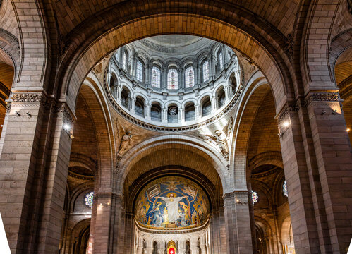 Interior view of the Basilica of the Sacred Heart of Montmartre showing the central dome with mosaics, the nave and colored stained glass windows in warm light, in Paris, France.