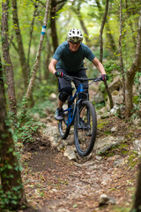 Naklejka premium Man mountain biking on a rocky forest trail wearing helmet and protective gear