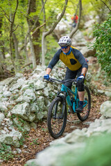 Naklejka premium Experienced male cyclist rides a teal mountain bike on a rocky forest trail