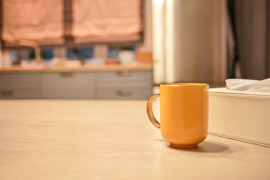 A yellow ceramic mug stands on a light table in the kitchen. Blurred background, soft light, the concept of breakfast, coziness and homely atmosphere. Yellow mug on the kitchen table, morning coffee
