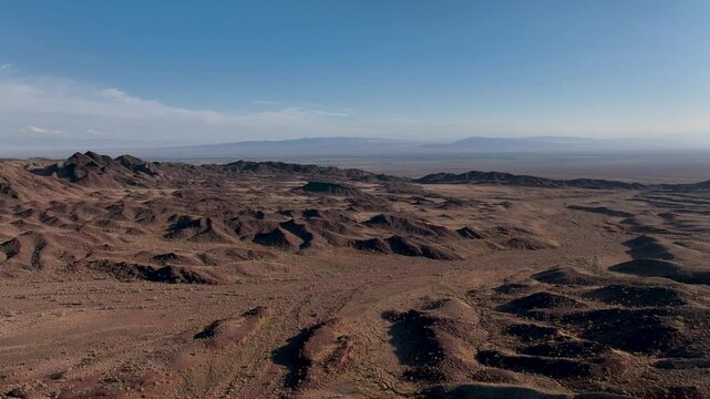 Drone soaring above brown volcanic Katutau mountain formations in Altyn Emel National Park, Kazakhstan. Aerial footage captures flight over rugged volcanic landscape with distinctive terrain features.