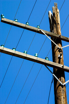 Wooden Utility Pole with Vintage Glass Insulators and Power Lines Against Blue Sky