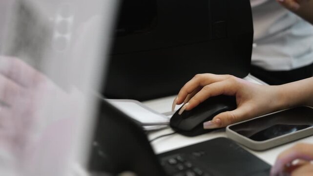Close up of office worker hand using computer mouse at desk with laptop and smartphone concept of data entry administrative work and business workflow indoors.