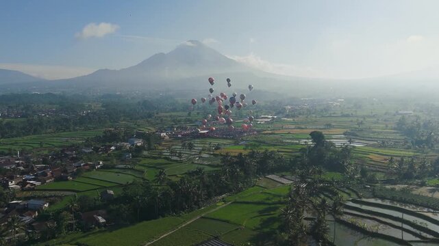 An epic wide aerial view of dozens of hot air balloons ascending gracefully above a vast green valley.Framed by a towering mountain and clear blue sky,the scene captures a breathtaking festival moment