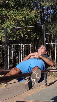 Athletic Middle Aged Man Doing Crunches on Parallel Bars - Calisthenics Park - Street Workout. Series Track Code: Fit-Mature-Man-54-Outdoor-Fitness-Series-2024