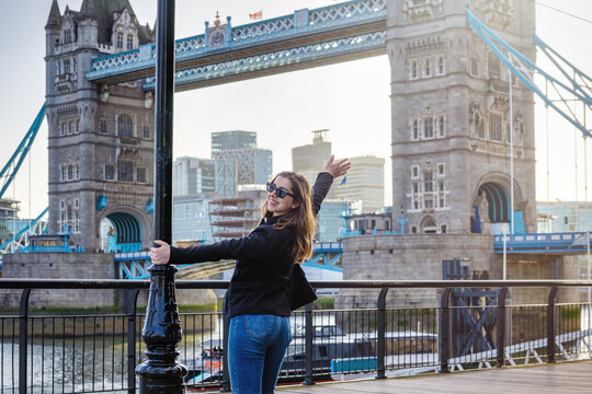 A excited, young woman stands in front of the Tower Bridge in London, England, during her sightseeing trip in the city