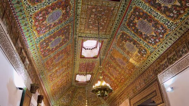 Interior of the Bahia Palace in Marrakech, Morocco, featuring ornate carved wooden ceilings and traditional chandeliers. Intricate moroccan architecture showcases colorful patterns.