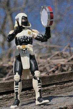 GI JOE Classified series action figure of Storm Shadow, in white hood and kawa-mono mask, beating on small marching snare drum. Birds nest, tree branches and blie skies in background, spring sunshine.