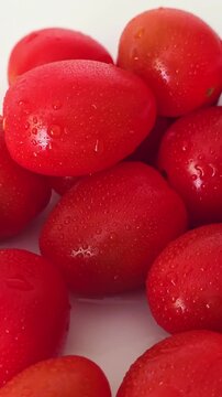 Water droplets cover ripe red tomatoes cerises on a table. vertical video.
