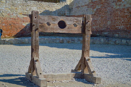 Historical wooden pillory stocks standing in the courtyard of Kazimierz Dolny castle ruins against ancient stone and brick walls in Poland under bright daylight