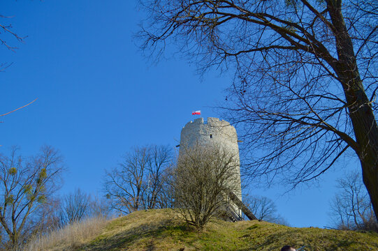 Historic stone castle tower known as Basta in Kazimierz Dolny with the Polish flag waving under a clear bright blue sky surrounded by trees