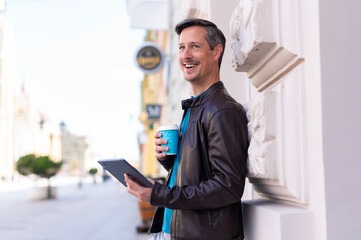 Happy man holding tablet and coffee cup in city © Dexon Dee