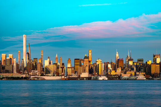 A wide panoramic view across the Hudson River shows the dense architecture of Manhattan during a colorful sunset in New York.