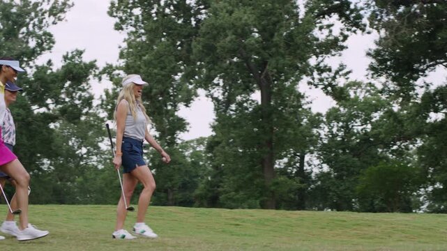 Three women walk with purpose across a lush golf course on a nice day.