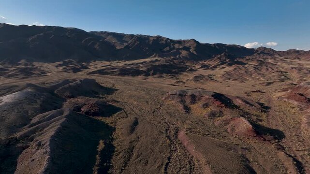 Drone camera flying over the volcanic mountains of Katutau in Altyn Emel National Park and turning toward the sun. Bright aerial scene with dramatic terrain and sunlight.