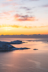 Fototapeta premium Golden sunset over a fjord on Kvaloya, Norway, with sun rays spreading above snow-covered mountains