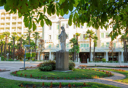 Abano, Italia - August 03, 2024: Statue of a Statua di Pietro d'Abano  surrounded by palm trees and landscaped gardens in front of a hotel building in a sunny setting