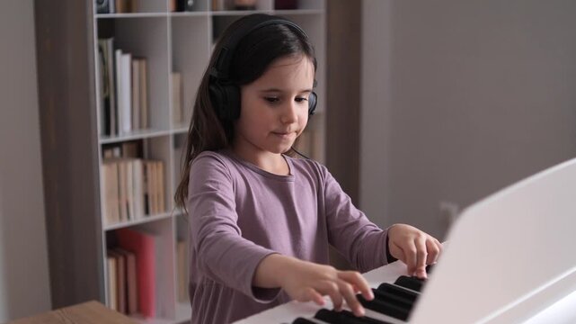 Young girl focusing intently on playing a modern digital piano, wearing headphones for concentrated practice while learning music in a home environment