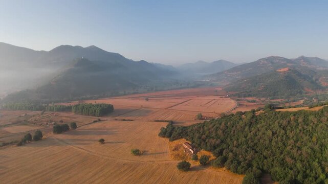 Aerial sunrise over agricultural fields and rolling hills near Kalavryta Greece, cinematic rural landscape with golden light, farmland patterns and mountain valley in soft morning haze