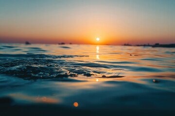 Naklejka premium Golden sun dips below horizon, casting orange glow on rippling water
