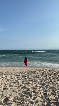 Female walking in red dress on sandy beach with waves and blue horizon enjoy peaceful in Rio de Janeiro Brazil lock down camera full body