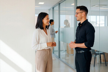 Fototapeta premium Professional man and woman smiling while talking in a bright minimalist coworking hallway with plenty of copy space for design.