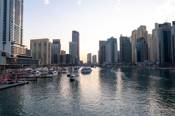 Obraz premium 12.12.2025 Dubai, UAE. Luxury yachts and boats moored in Dubai Marina at sunset. Stunning view of skyscrapers and modern architecture in UAE with golden sky reflection in the water. High-end lifestyle