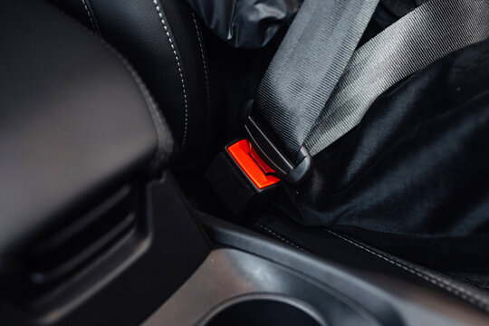 Close-up view of a car seatbelt buckle and strap secured in a modern vehicle interior with leather upholstery and cup holder visible in the foreground