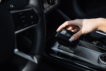 Fototapeta premium Driver's hand operating gear shift in modern car interior, showcasing sleek dashboard design and high-quality materials in a contemporary vehicle setting