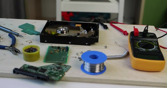 Tech repair workspace showcases tools and equipment. Various electronic components lie on wooden surface. Focus on hard drive and multimeter for precise diagnostics. Small business.