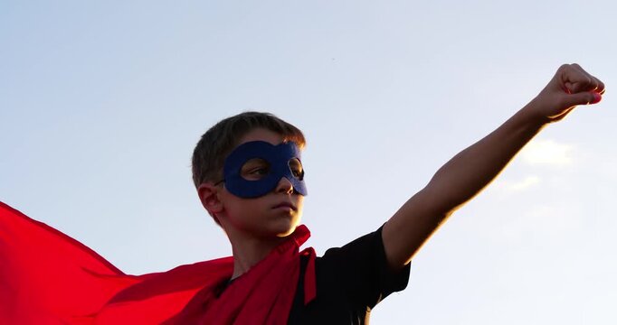 Child embodies superhero confidence with cape and mask. Young boy expresses bravery and imagination while wearing vibrant red cape. Scene captures playful adventure and creativity.
