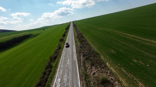 FPV drone footage flying above vast green farmland, tracking a straight rural highway and intersection stretching to the horizon; minimalist aerial landscape under clear sky.