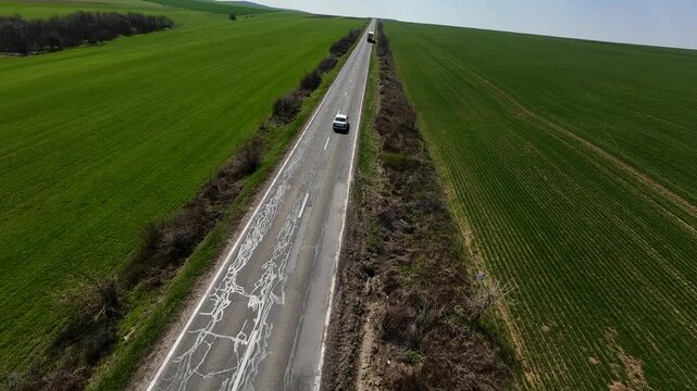 FPV drone footage flying above vast green farmland, tracking a straight rural highway and intersection stretching to the horizon; minimalist aerial landscape under clear sky.