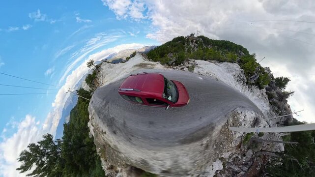 Tiny planet effect featuring a red car on a dirt road surrounded by white rocky cliffs, green trees, and a blue sky with clouds, creating a surreal, circular perspective. Unique Mountain Road