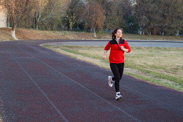 Fototapeta premium Fit mid adult woman 40s running on an outdoor track, wearing a vibrant red sports uniform