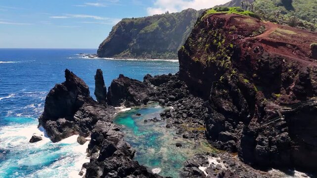 Aerial Drone footage of Pitcairn Islands Over Clear Blue Ocean. Volcanic coast ocean showcasing rugged green slopes, basalt cliffs, scattered village houses, crashing white waves over coral