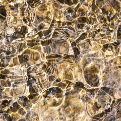 Cotignac, Provence-Alpes-Côte d’Azur, France : abstract golden light patterns in clear shallow water over natural stones, textured background
