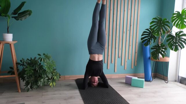 Young athletic woman doing headstand or salamba sirsasana position in yoga studio or at home