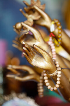 Close-up of multiple golden hands of multi-armed Guanyin statue with various mudras and mala beads.
