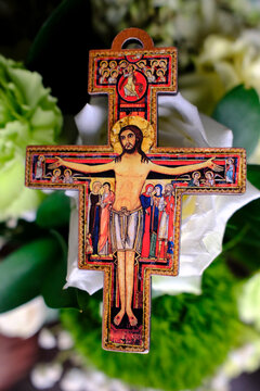 Miniature San Damiano cross wooden icon of Christ crucified against soft floral background.