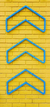 Blue Arrow Direction Symbols on Yellow Brick Wall &ndash; Modern Minimal Geometric Background