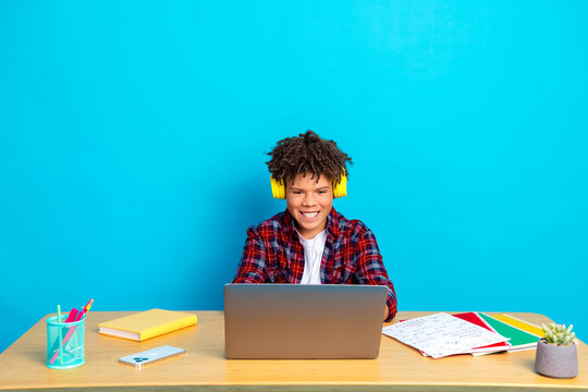 Smiling student wearing headphones studying on a laptop at a colorful desk for online learning and remote schoolwork