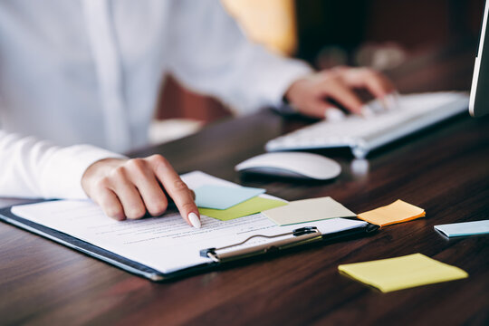 Businesswoman reviewing documents at office desk with clipboard, sticky notes and computer while working on paperwork and planning tasks