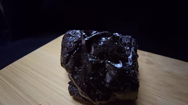 Cinematic macro shot of raw black Shilajit resin with a glossy, glass-like luster. This organic mineral exuding from Himalayan rocks features a dark, reflective texture and mysterious aesthetic.