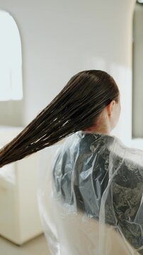 A woman gets her hair done in a salon. Her stylist combs her long, wet hair in preparation for a haircut. The salon is clean, modern, and has good lighting. The focus is on hair care, beauty,