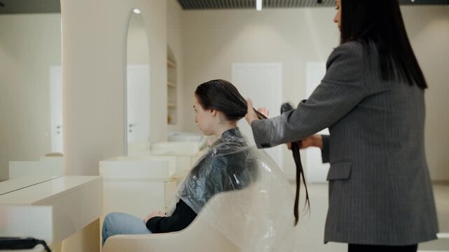 A hair stylist combs her client's wet hair in a beauty salon. The stylist prepares the client's hair for a treatment or styling. The salon is modern, clean, and has a relaxing atmosphere.
