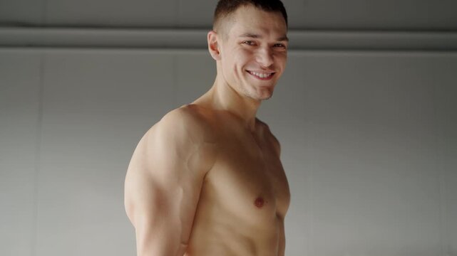 Portrait of a fit young man with a subtle smile, showcasing his well-defined muscles in a bright modern gym environment. Young Athletic Man Smiling Confidently in Modern Gym Setting